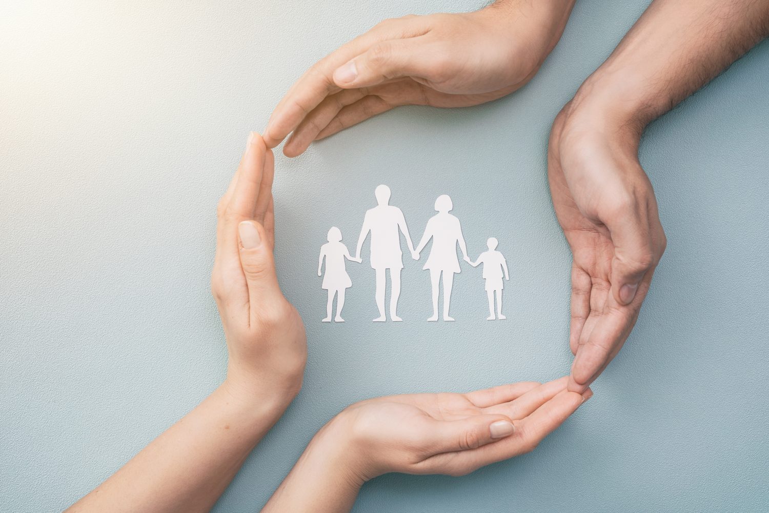 Hands circling a paper cut-out of a family